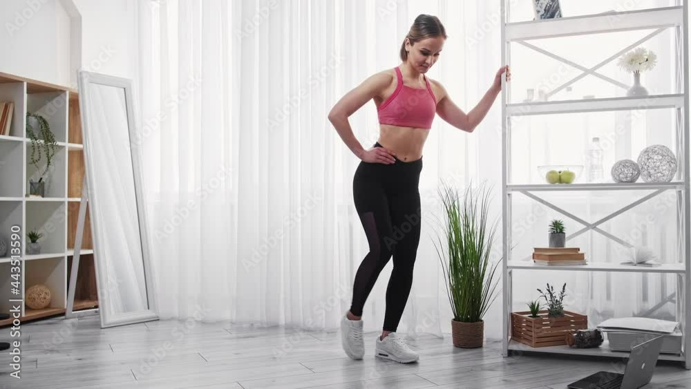 Female fitness. Sport indoors. Home workout. Fat burning. Happy sporty young woman athlete in activewear doing leg exercise in light apartment interior. Female fitness. Sport indoors. Home workout. Fat burning. Happy sporty young woman athlete in activewear doing leg exercise in light apartment interior.