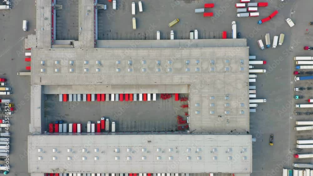 Aerial top down view of a logistics park with a large warehouse and a loading hub. A lot of semi-trailer trucks standing at ramps for load and unload goods