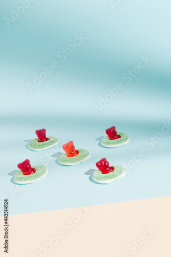 Creative minimal composition of red gummy bears and green gummy rings on the pastel blue and beige background.