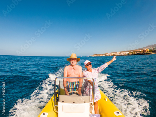 Beautiful and cute couple of seniors or old people in the middle of the sea driving and discovering new places with small boat. Mature woman holding a phone and taking a selfie with hew husband.