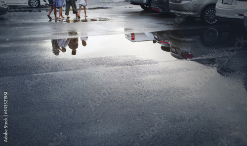 Wet parking spaces after hard rain fall with reflection of cars and walking people in puddle on the ground .Selective focus.