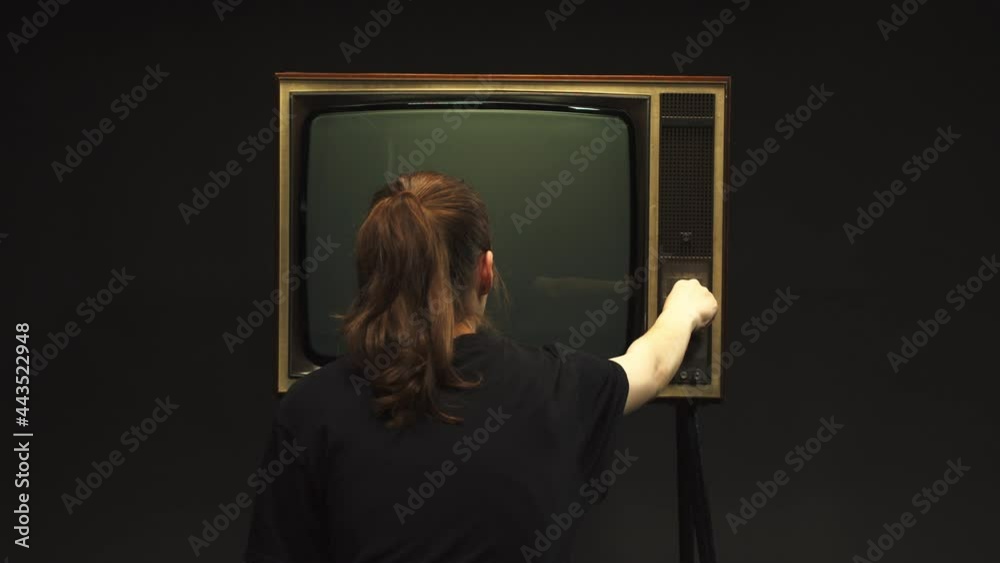 Young woman setting up channel on old retro television on black background, searching for a