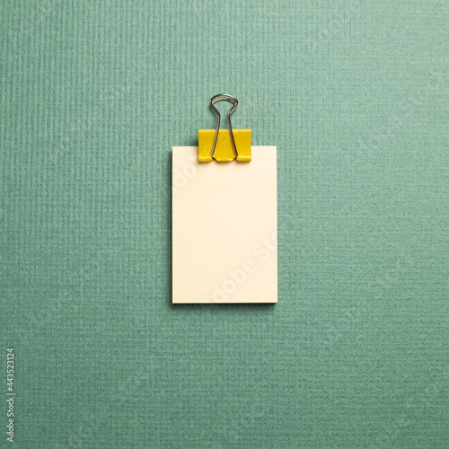 Blank memo pad with yellow metal clip on green background. top view, copy space