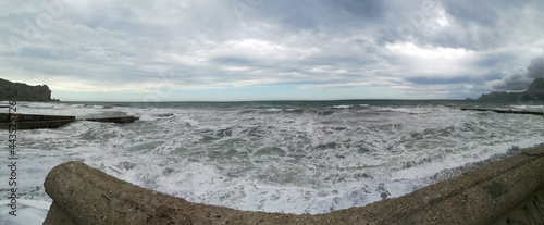 Thunderclouds and large foaming waves during a storm at sea. Cyclone, bad weather, meteorology, climate change, natural phenomenon. Panorama. Sudak, Crimea.