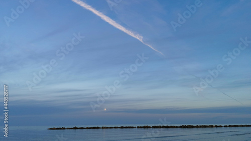 Cielo sopra il mare al tramonto nuvole scie e luna sulla scogliera