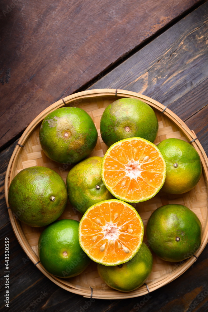 Green tangerine orange fruit in a bamboo basket on wooden background, Table top view Green tangerine orange fruit in a bamboo basket on wooden background, Table top view