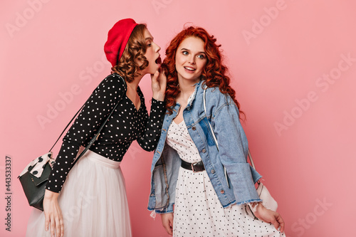 Curly girls in casual outfit talking on pink background. Studio shot of refined friends sharing rumours.