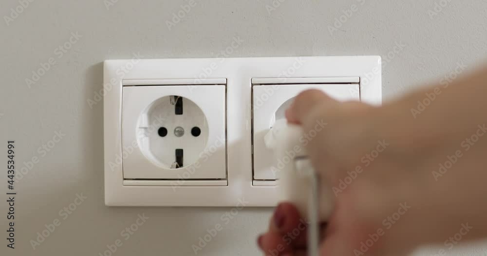Woman's hand plugging white power plug into white multiple socket indoors.