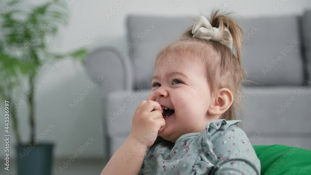 babyhood, smiling female child with appetite eats ripe grapes for snack and laughs while sitting on background of sofa in living room babyhood, smiling female child with appetite eats ripe grapes for snack and laughs while sitting on background of sofa in living room