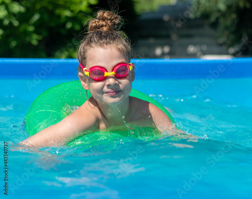 A little girl is swimming in the pool, wearing diving glasses, a swimming circle. Summer vacation, sunny day