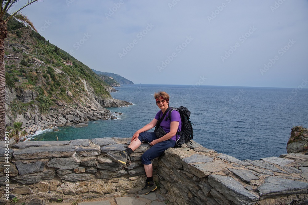Senior woman sitting on stone wall with seascape in background