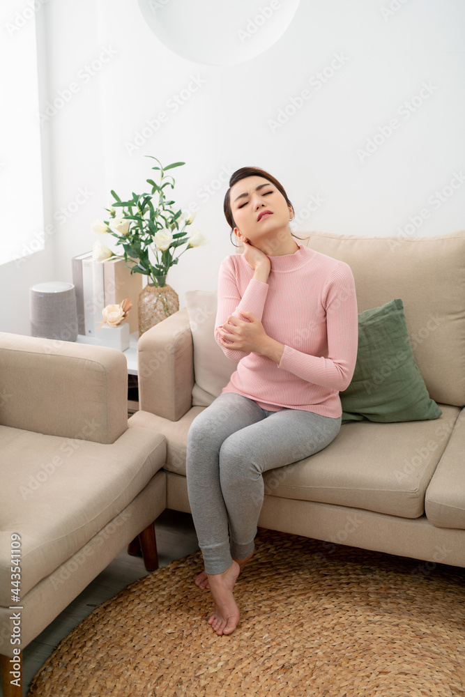 Young woman sitting on sofa with neck pain at home. Young woman sitting on sofa with neck pain at home.