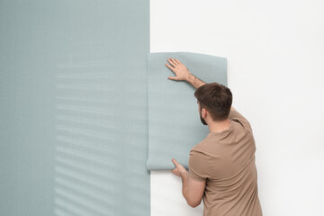Man hanging stylish wall paper sheet. Space for text
