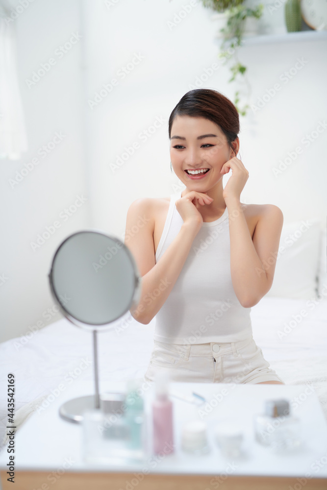Image of pleased asian woman smiling and looking at mirror Image of pleased asian woman smiling and looking at mirror