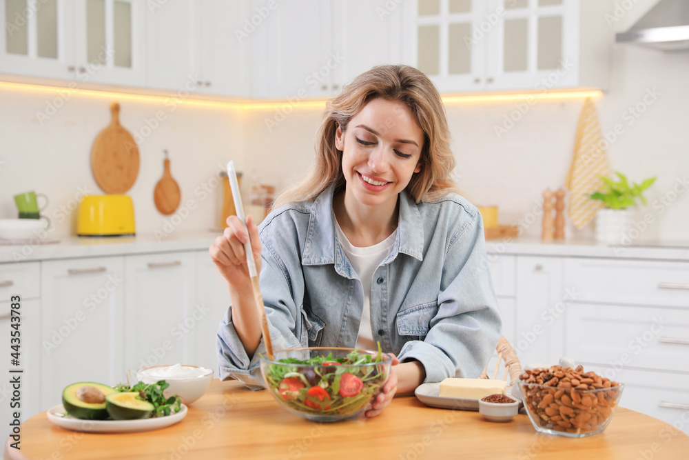 Woman with salad at wooden table in kitchen. Keto diet