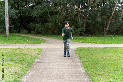 Active tyung boy running in park towards camera. Fitness and training concept. Athletic boy running on concrete path at park.