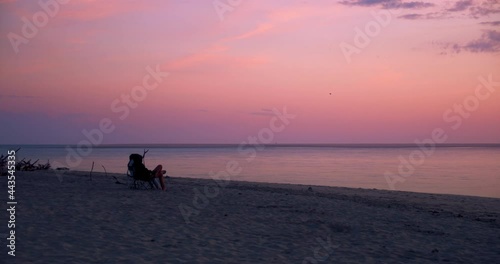 Two people sitting on chairs on beach at dusk. Colorful pink and purple sky photo