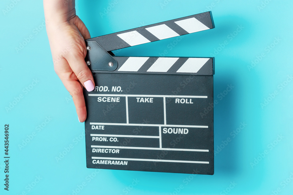 Female hand holding movie clapper board close-up on blue background.