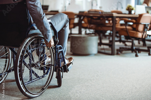 Paralyzed man in a wheelchair on the move in the disabled office building. Wheeling his way into recovery. Businessman hand driving wheelchair. Businessman on wheelchair