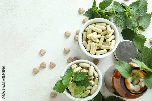 Nettle pills and ingredients on white textured table