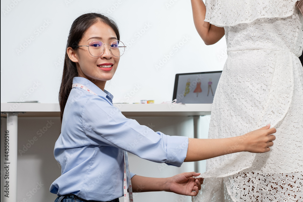 Naklejka premium Beautiful young Asian fashion tailor with textile sewing accessories and entrepreneur designer sketches are full of bright colors on the desk with a laptop for creative ideas in the studio