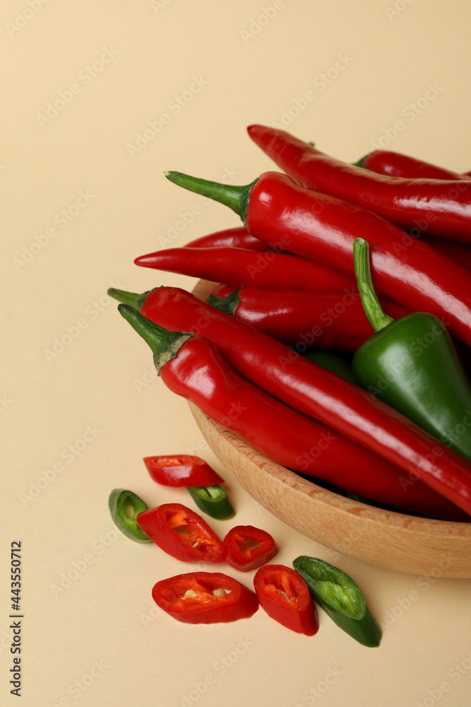 Bowl with red and green hot peppers on beige background