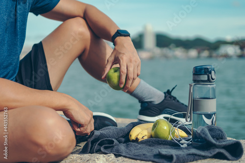 Healthy man hold apple fruit and sitting on the stone near the beach.