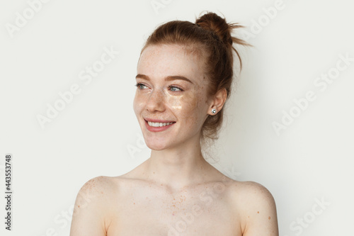 Photographie Adorable ginger woman with freckles is smiling on a white studio wall wearing tr