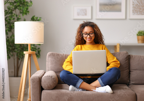 Smiling african american young woman using laptop while working remotely or studying online from home