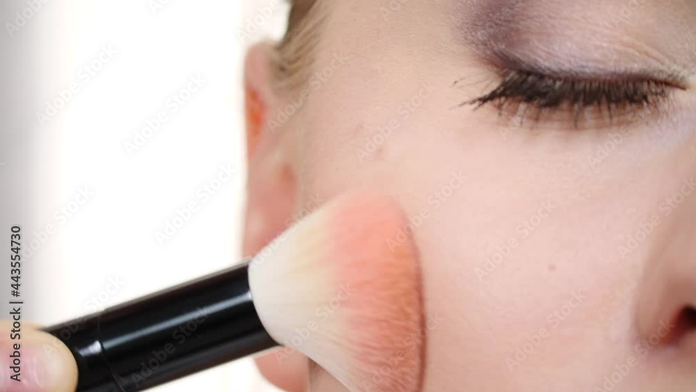 Woman face painting. Makeup artist applying blush bronzer with brush to model cheek. Cosmetic beauty procedures and makeover concept. Slow motion Woman face painting. Makeup artist applying blush bronzer with brush to model cheek. Cosmetic beauty procedures and makeover concept. Slow motion