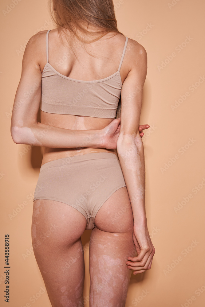 Woman is boasting of her figure while posing at the studio with beige background