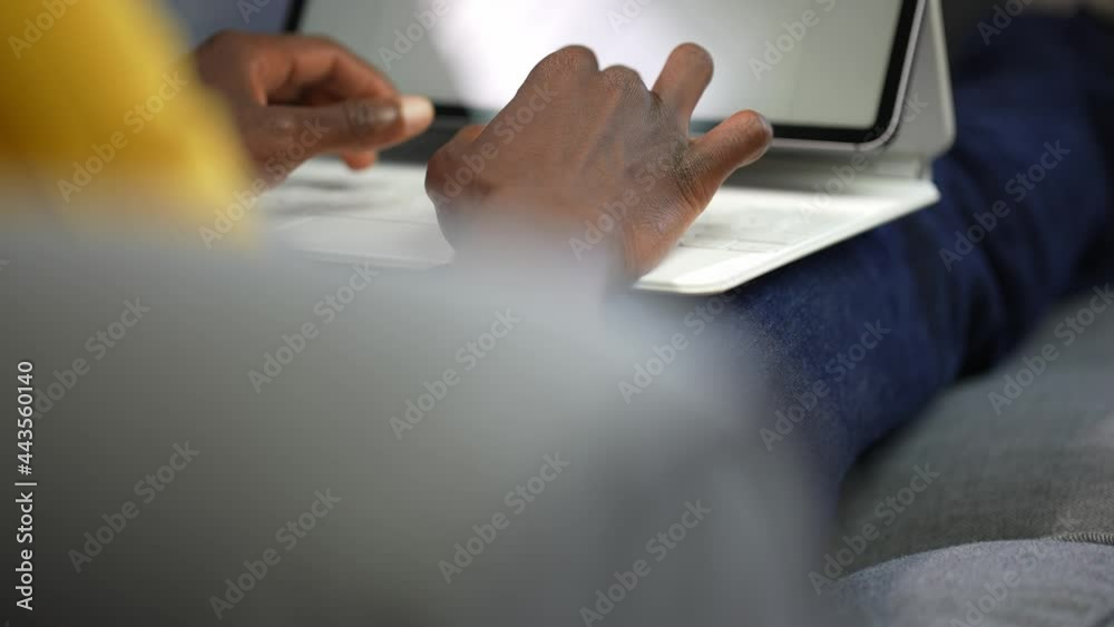 POV shot of black afro-american man's hands typing on a white laptop or tablet keyboard resting on his knees. 