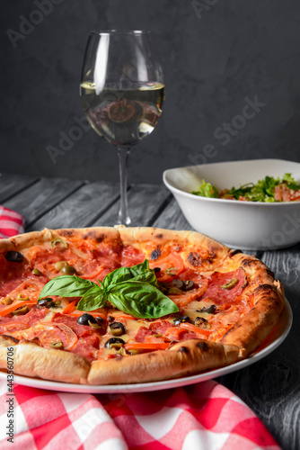 Fresh italian pizza with salami and black olives served with a glass of white wine.