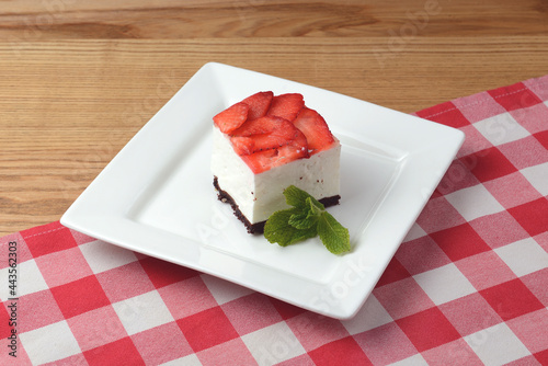 Strawberry cheesecake and fresh strawberries on top served on white plate on a rustic wooden table photo