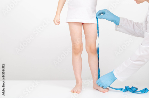 A doctor in blue gloves with a measuring tape measures the length of the legs of a 4-year-old caucasian girl. Child development and growth concept. Copy space for text
