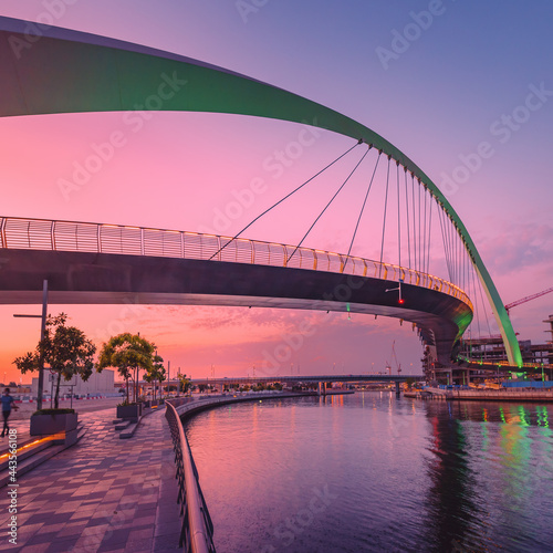 Fototapeta Naklejka Na Ścianę i Meble -  Tolerance bridge and promenade embankment along Dubai Creek Canal during majestic colorful sunset light