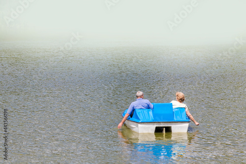An old couple in love are relaxing on a water bike. A view from the back with a copy of the space at the top.