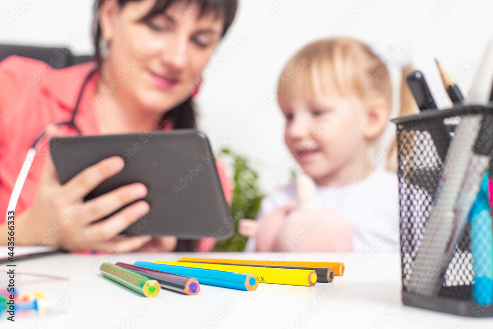 Caucasian woman child doctor shows cartoons on the tablet to a little girl 4 years old. The concept of doctors' approach to children Caucasian woman child doctor shows cartoons on the tablet to a little girl 4 years old. The concept of doctors' approach to children