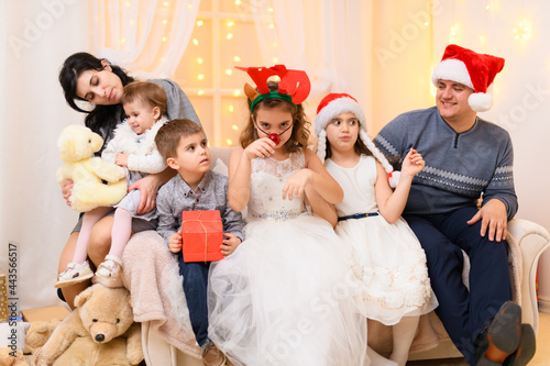 happy big family portrait - parents and children in home interior decorated with holiday lights and gifts, dressed in santa hat for new year celebration