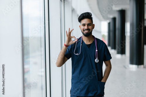 Indian doctor man smiling and holding fingers as okay gesture with clinic