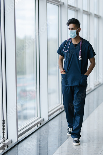 Portrait of a smiling Asian Indian male medical doctor standing inside hospital.