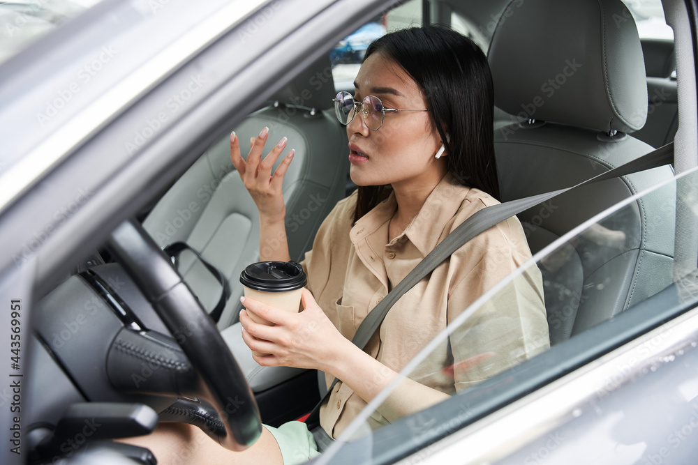 Woman drinking coffee and telling something emotionally while driving a car Woman drinking coffee and telling something emotionally while driving a car