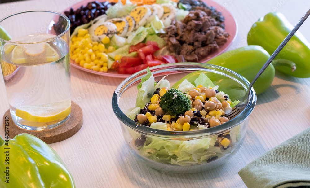 Salads with mix of fresh vegetables. Green paprika and glass of water with lemon on the table. Healthy concept Salads with mix of fresh vegetables. Green paprika and glass of water with lemon on the table. Healthy concept