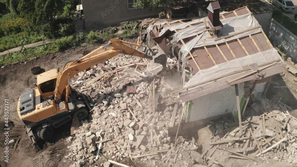 Demolition of house building for new construction by excavator bucket, aerial view. City development.
