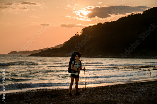 young smiling woman tourist on the seashore against the backdrop of mountains and sunset