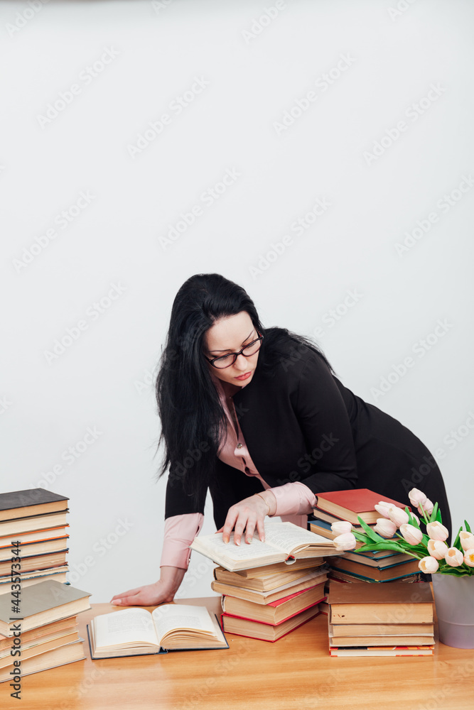 beautiful female teacher in business suit at a table with stacks of educational books beautiful female teacher in business suit at a table with stacks of educational books