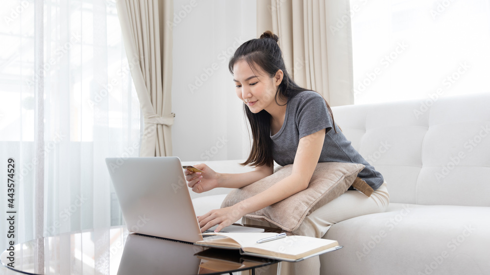 Asian woman sitting on sofa and using laptop to shop online with credit card to register for payment or online transactions, Financial transactions and Internet security, Shopping with credit card. Asian woman sitting on sofa and using laptop to shop online with credit card to register for payment or online transactions, Financial transactions and Internet security, Shopping with credit card.