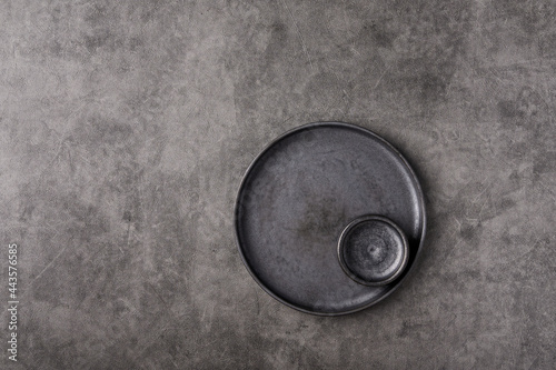 Empty dark plate with saucer set on gray graphite textured background. Top view, copy space