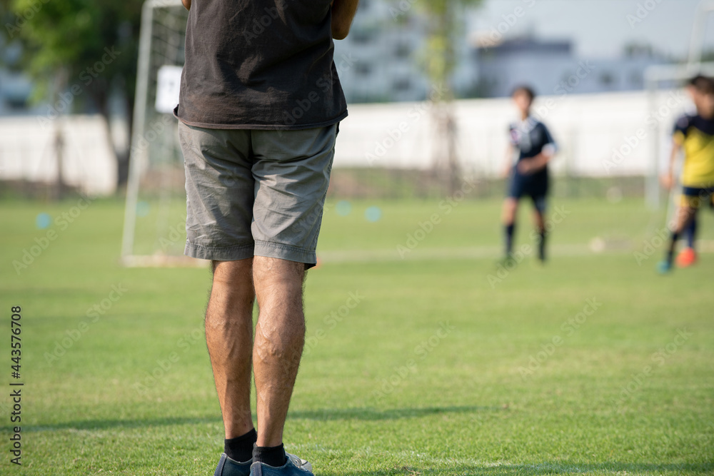 Father standing and watching his son playing football in a school tournament on a clear sky and sunny day. Sport, active lifestyle, happy family and soccer mom and dad concept. Father standing and watching his son playing football in a school tournament on a clear sky and sunny day. Sport, active lifestyle, happy family and soccer mom and dad concept.