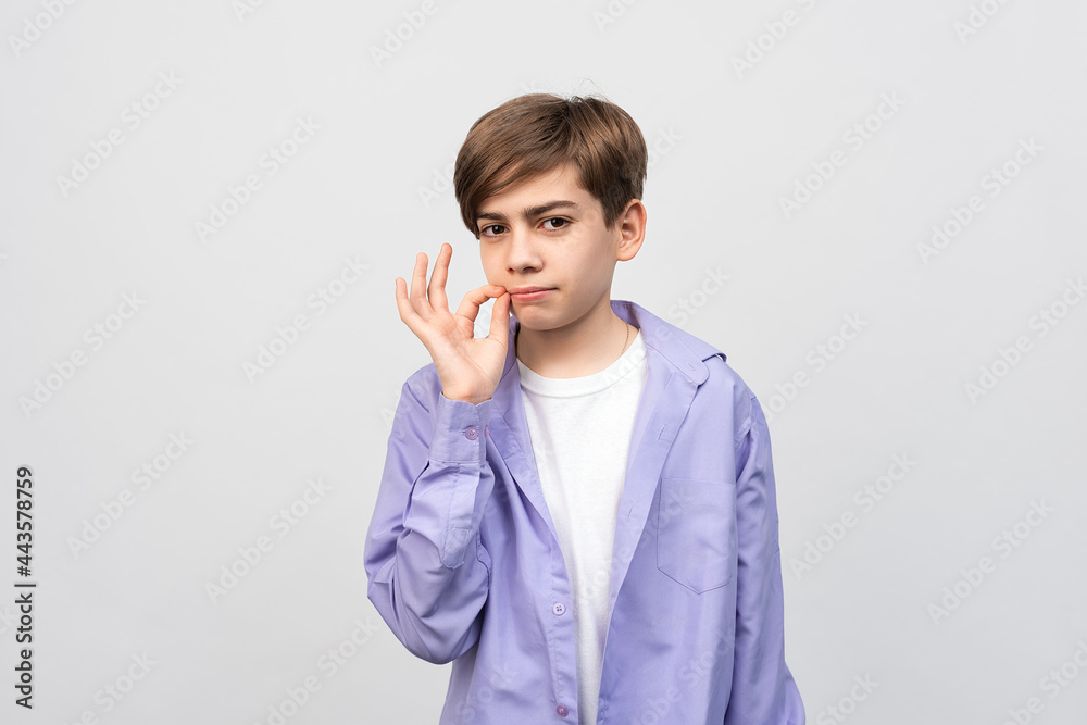 Shh its secret. Portrait of serious boy showing zip gesture as if shutting mouth on key, promises to keep secret, gray background, isolated Shh its secret. Portrait of serious boy showing zip gesture as if shutting mouth on key, promises to keep secret, gray background, isolated